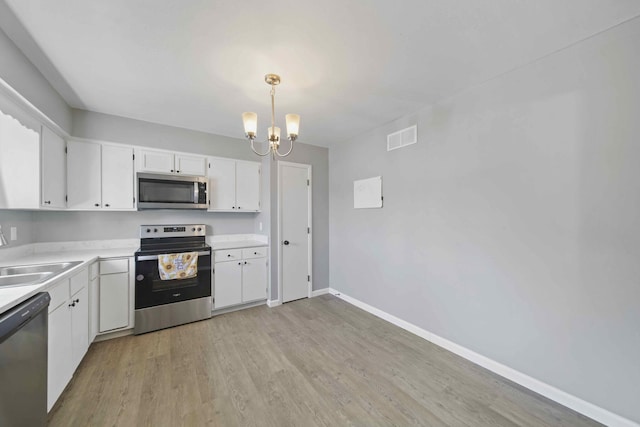 kitchen featuring sink, white cabinetry, hanging light fixtures, stainless steel appliances, and a notable chandelier