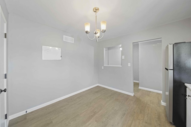 unfurnished dining area with a notable chandelier and light hardwood / wood-style floors