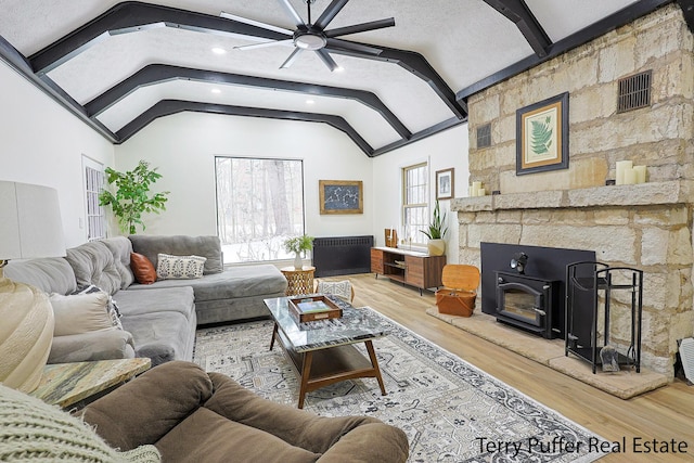 living room featuring vaulted ceiling with beams, a textured ceiling, a wood stove, ceiling fan, and hardwood / wood-style floors