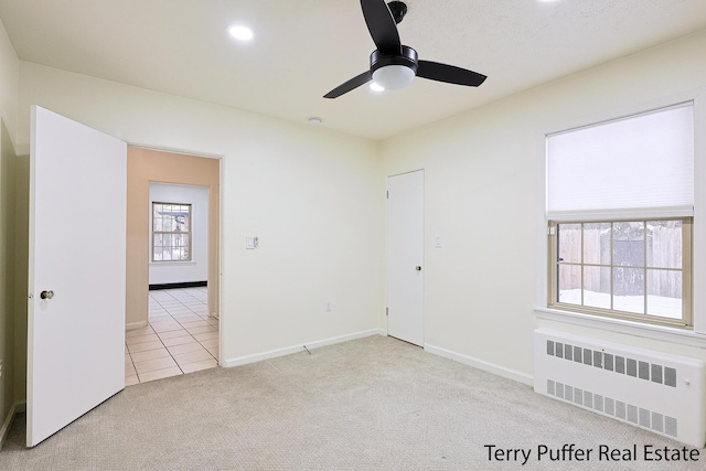 carpeted empty room featuring ceiling fan and radiator