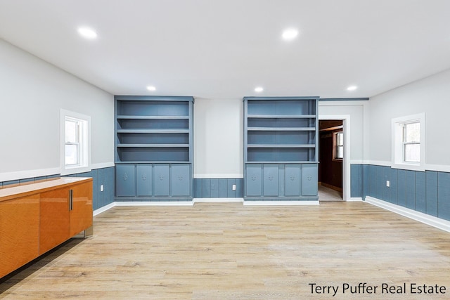 unfurnished living room with a wealth of natural light, built in features, and light hardwood / wood-style flooring