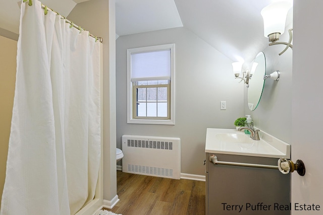 bathroom featuring radiator heating unit, lofted ceiling, hardwood / wood-style flooring, vanity, and walk in shower