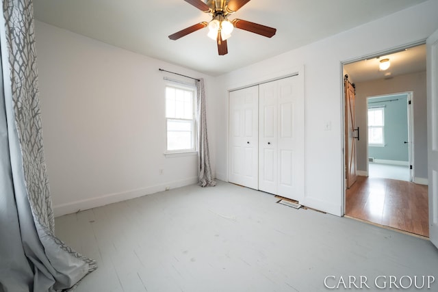 unfurnished bedroom with ceiling fan, a closet, wood-type flooring, and multiple windows