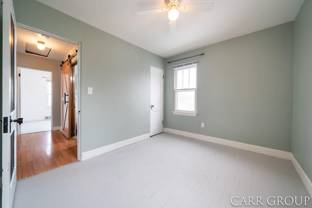 empty room with a barn door, light wood-type flooring, and ceiling fan