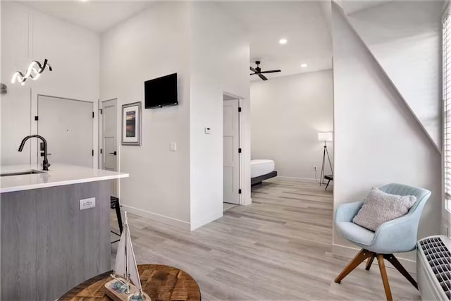 kitchen featuring sink, decorative light fixtures, light wood-type flooring, ceiling fan, and a high ceiling