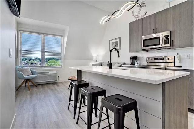 kitchen with sink, light hardwood / wood-style flooring, stainless steel appliances, a kitchen breakfast bar, and an island with sink