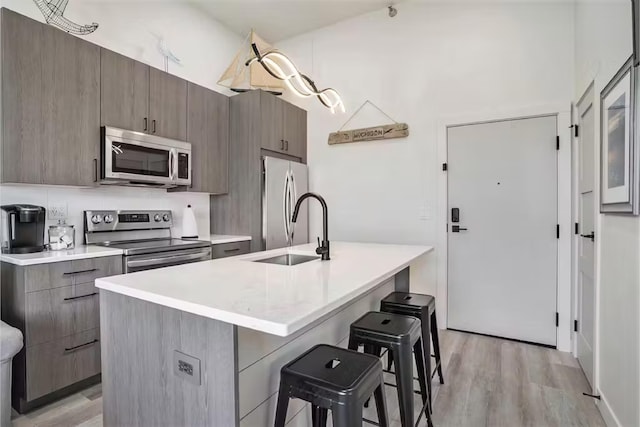 kitchen with a breakfast bar, sink, a kitchen island with sink, stainless steel appliances, and light hardwood / wood-style floors