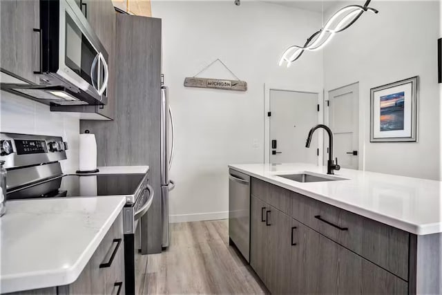 kitchen featuring sink, light hardwood / wood-style flooring, appliances with stainless steel finishes, dark brown cabinetry, and a center island with sink