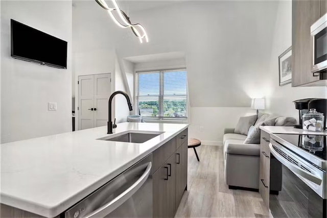 kitchen with appliances with stainless steel finishes, a kitchen island with sink, sink, and light wood-type flooring