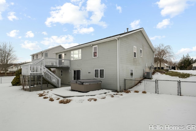 snow covered property with a wooden deck, central AC unit, and a hot tub