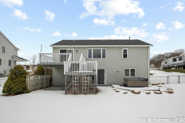 snow covered back of property with a wooden deck and a hot tub