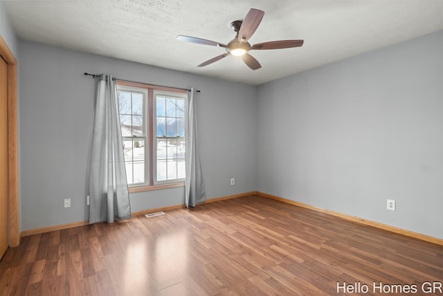 empty room with ceiling fan, wood-type flooring, and a textured ceiling