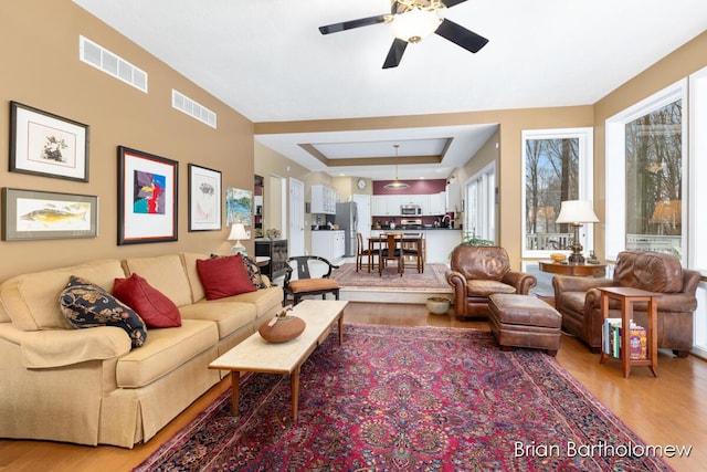 living room featuring wood-type flooring, a raised ceiling, and ceiling fan