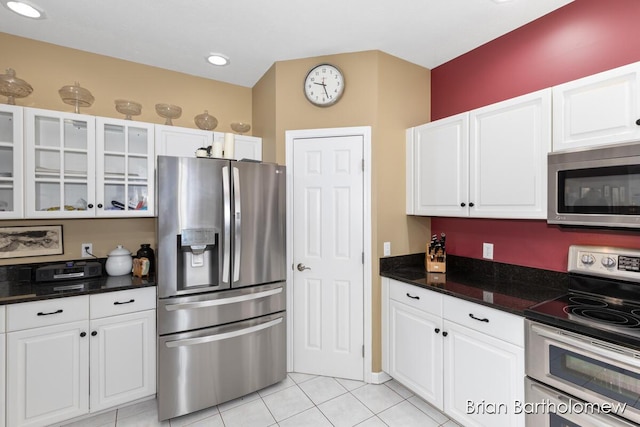 kitchen with dark stone countertops, appliances with stainless steel finishes, light tile patterned floors, and white cabinets