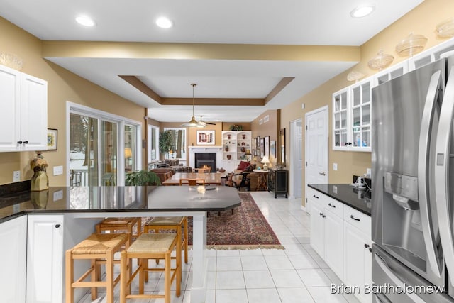 kitchen featuring light tile patterned floors, white cabinetry, stainless steel refrigerator with ice dispenser, a kitchen bar, and a raised ceiling