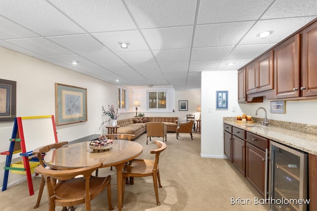 carpeted dining space with a drop ceiling, wet bar, and beverage cooler