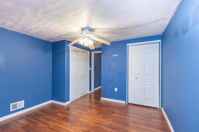 unfurnished bedroom featuring multiple closets, dark wood-type flooring, a textured ceiling, and ceiling fan