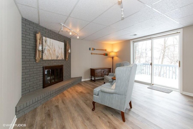 sitting room featuring light wood finished floors, a drop ceiling, rail lighting, and a brick fireplace