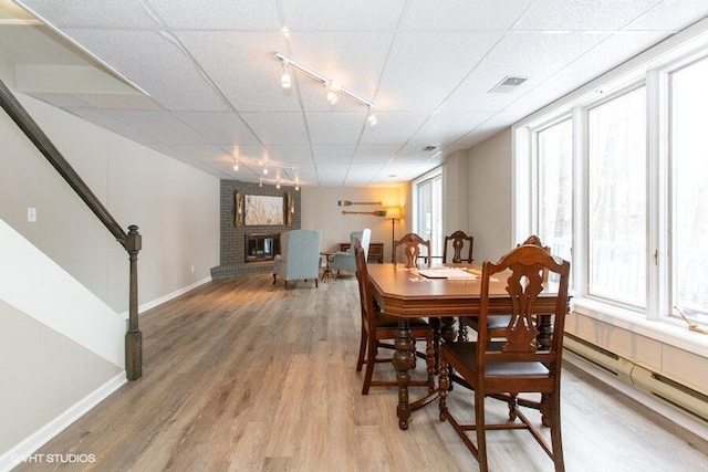 dining area with wood finished floors, baseboards, stairs, a brick fireplace, and track lighting