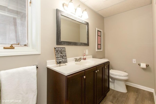 half bathroom with toilet, wood finished floors, vanity, and baseboards