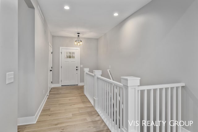 corridor featuring recessed lighting, light wood-style flooring, an inviting chandelier, baseboards, and an upstairs landing