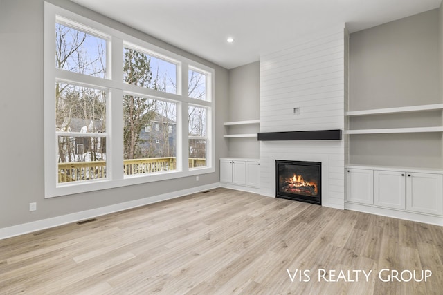 unfurnished living room with baseboards, visible vents, a large fireplace, and light wood-style floors