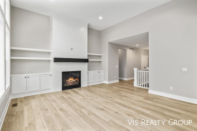 unfurnished living room featuring baseboards, visible vents, a fireplace, light wood-type flooring, and built in shelves