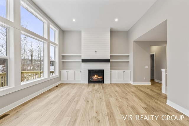 unfurnished living room with a large fireplace, visible vents, baseboards, built in features, and light wood-style floors