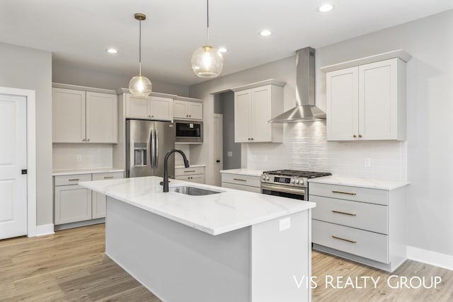 kitchen featuring appliances with stainless steel finishes, hanging light fixtures, a kitchen island with sink, wall chimney range hood, and a sink