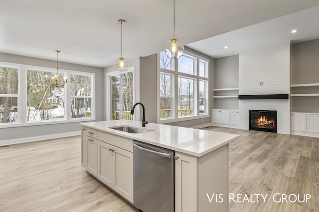 kitchen with a sink, light countertops, pendant lighting, an island with sink, and stainless steel dishwasher