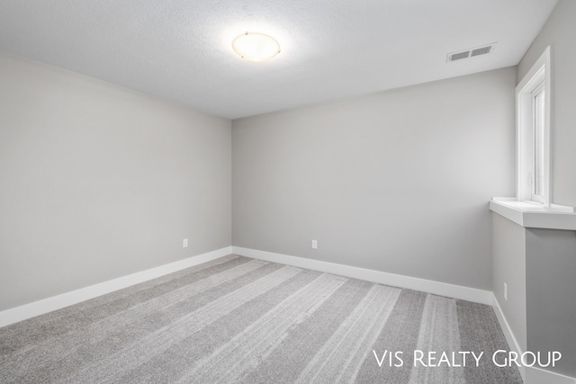 carpeted spare room featuring baseboards, visible vents, and a textured ceiling