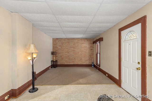 foyer with a drop ceiling, light carpet, and brick wall