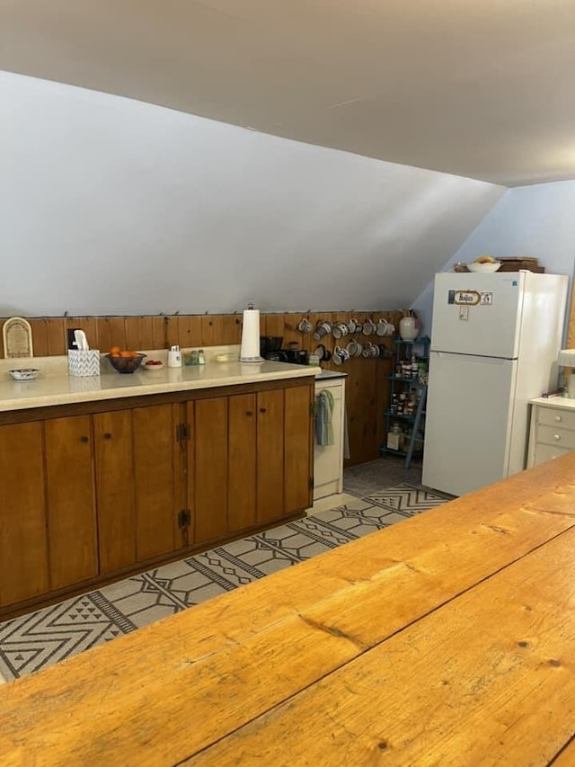 kitchen with brown cabinetry, lofted ceiling, freestanding refrigerator, light countertops, and light floors