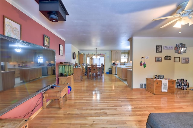 living room with sink, ceiling fan with notable chandelier, light hardwood / wood-style flooring, and ornamental molding