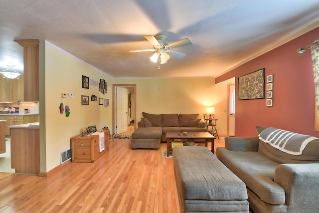 living room featuring ceiling fan, ornamental molding, and light wood-type flooring