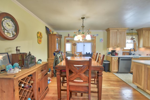 dining room with an inviting chandelier, sink, ornamental molding, and light wood-type flooring