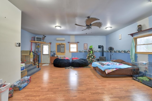 bedroom with ceiling fan, a wall unit AC, and light hardwood / wood-style flooring