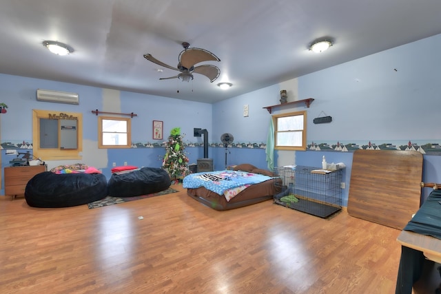 bedroom with hardwood / wood-style flooring, a wood stove, a wall mounted AC, and ceiling fan