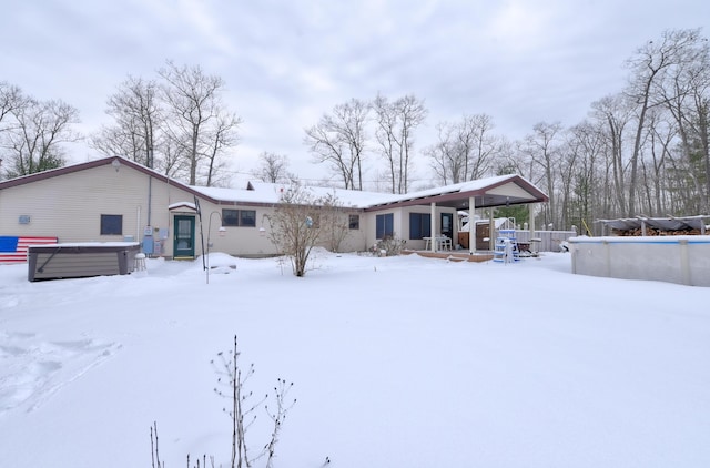 snow covered rear of property featuring a hot tub