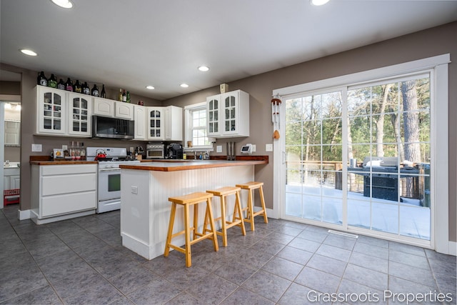 kitchen featuring white gas range oven, a breakfast bar, white cabinetry, tile patterned floors, and kitchen peninsula