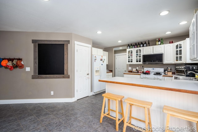 kitchen with a breakfast bar, sink, kitchen peninsula, white appliances, and white cabinets