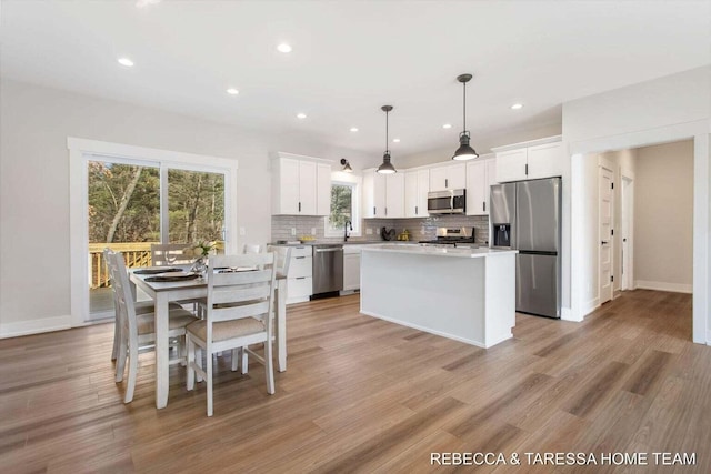 kitchen with a center island, appliances with stainless steel finishes, white cabinets, pendant lighting, and backsplash