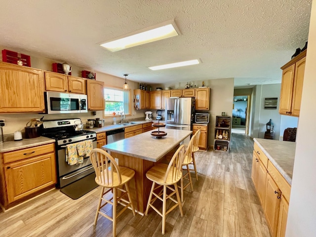 kitchen with sink, a breakfast bar, appliances with stainless steel finishes, a center island, and light hardwood / wood-style floors