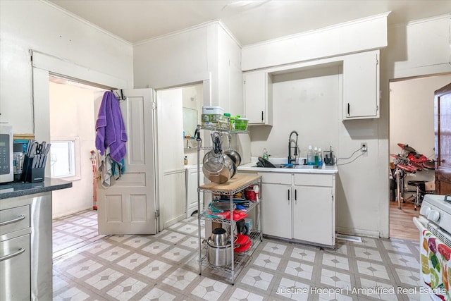 kitchen featuring sink, crown molding, white gas range oven, white cabinetry, and washer / dryer