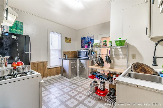 kitchen with sink, gas range gas stove, wood walls, black refrigerator, and white cabinets