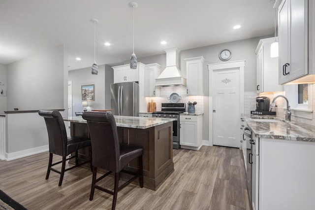 kitchen featuring a kitchen bar, white cabinetry, a center island, custom range hood, and stainless steel appliances