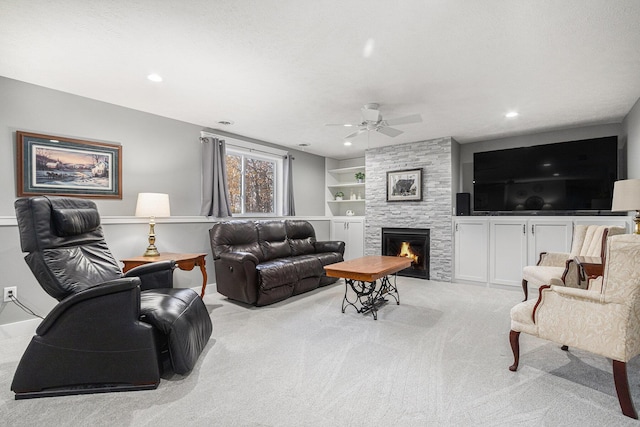 carpeted living room with ceiling fan, a stone fireplace, built in features, and a textured ceiling