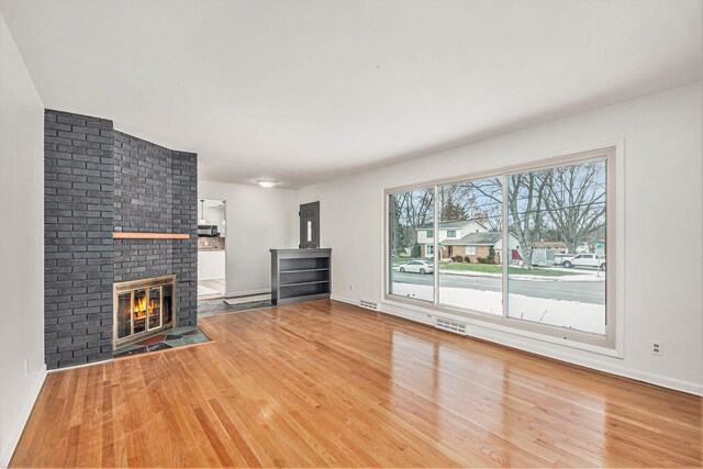 unfurnished living room featuring wood-type flooring and a brick fireplace