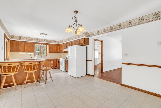 kitchen with white appliances, an inviting chandelier, hanging light fixtures, a kitchen breakfast bar, and kitchen peninsula