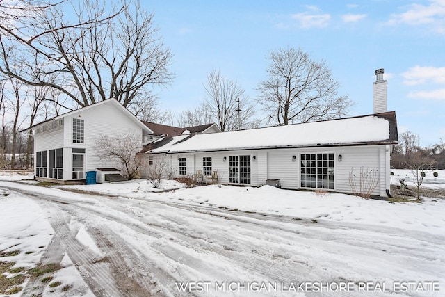 snow covered back of property featuring a sunroom